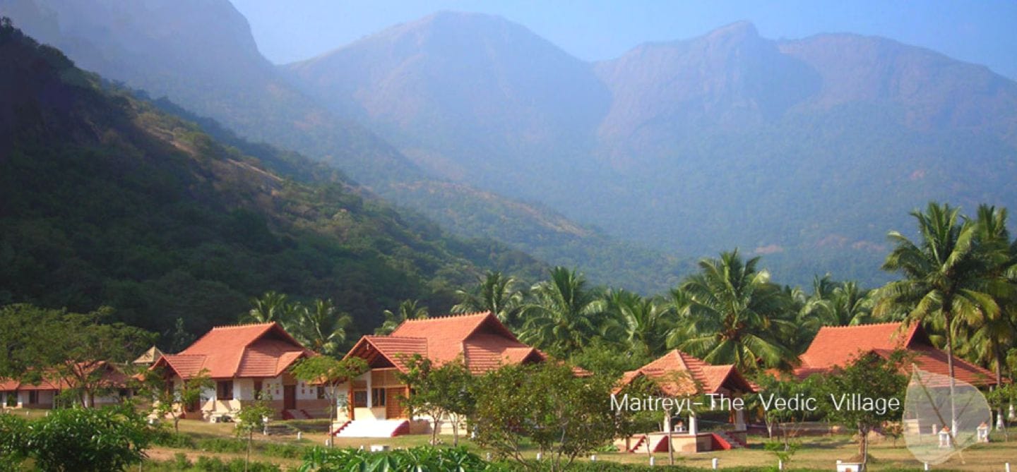 Maitreyi Vedic Village cottages with terracotta roofs, palm groves, and mountains behind